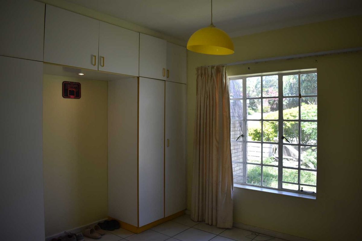 A bedroom featuring built-in white cabinetry with overhead storage and a window overlooking the garden.
