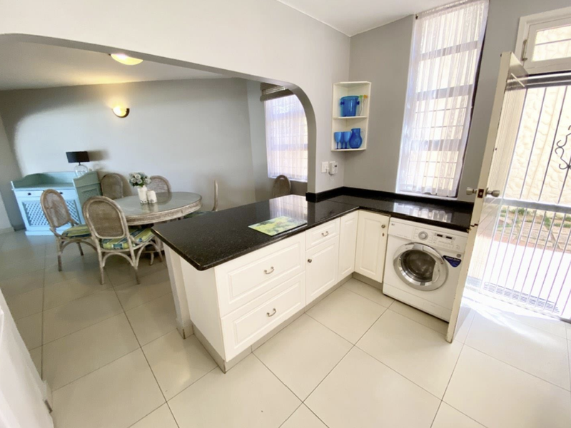Open plan kitchen and dining area featuring white cabinetry, dark granite countertops, integrated laundry appliance, and tiled flooring with an arched transition.