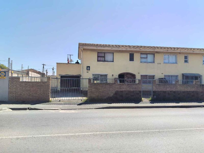 Front elevation of a townhouse featuring a brick boundary wall, metal security gates, and a garage, showing signs of exterior wear.