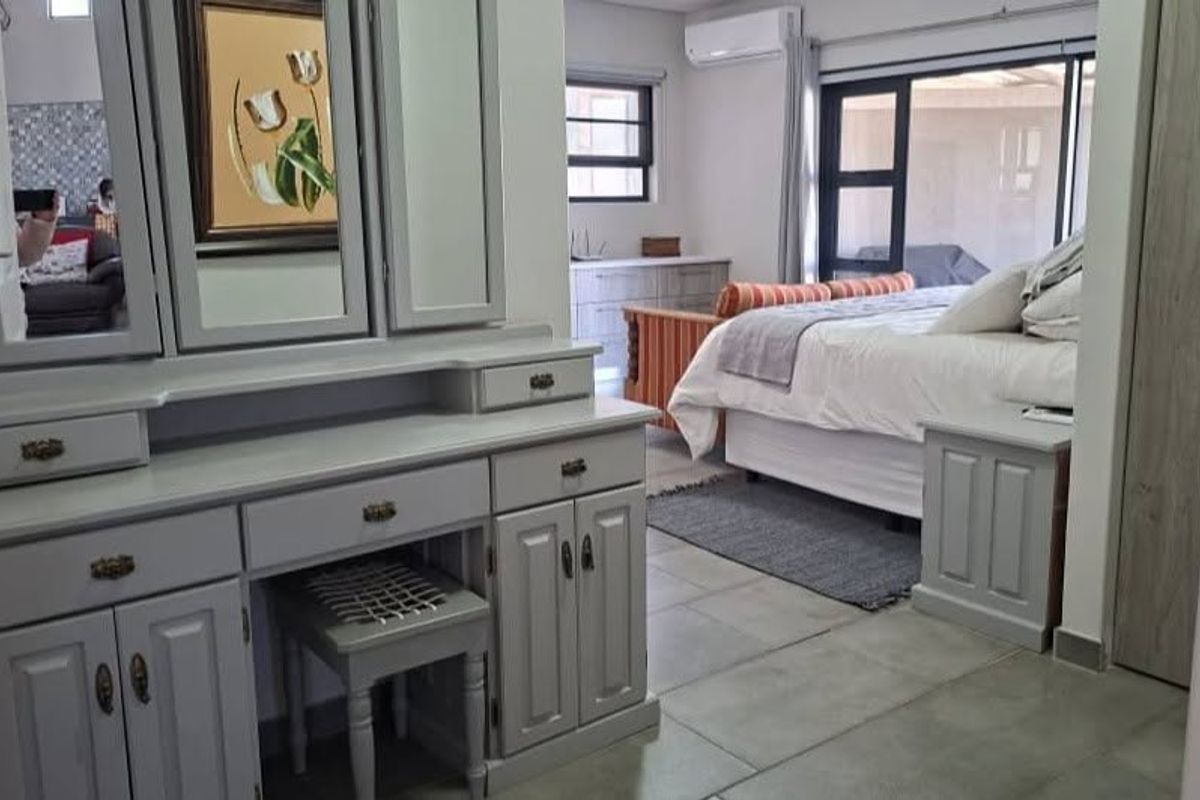 Spacious bedroom featuring tiled flooring, built-in vanity, integrated cupboards, and an air conditioning unit with access to an outdoor area via sliding glass doors.