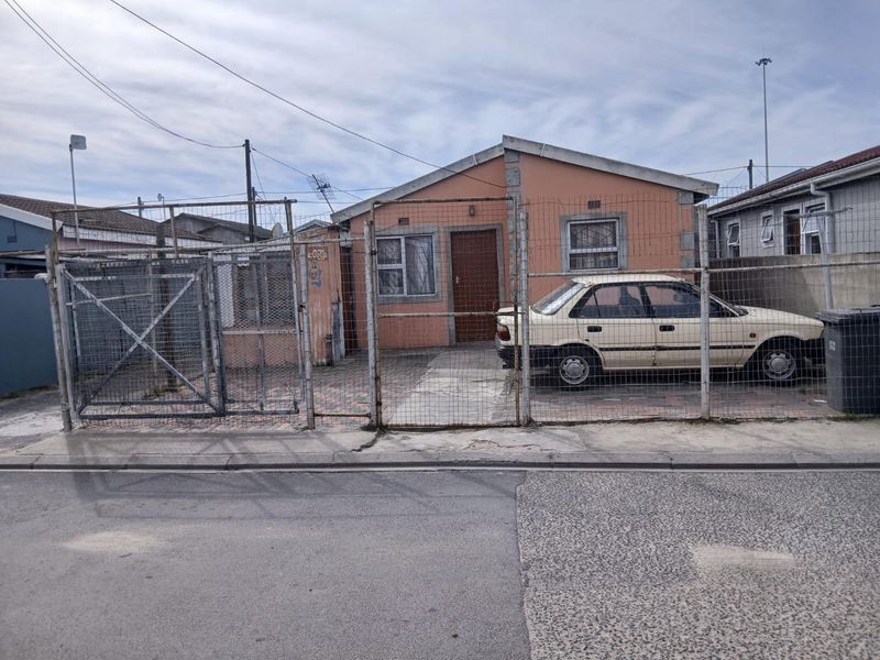 Front elevation of a single-story house featuring a paved driveway, security fencing, and security bars on the windows.