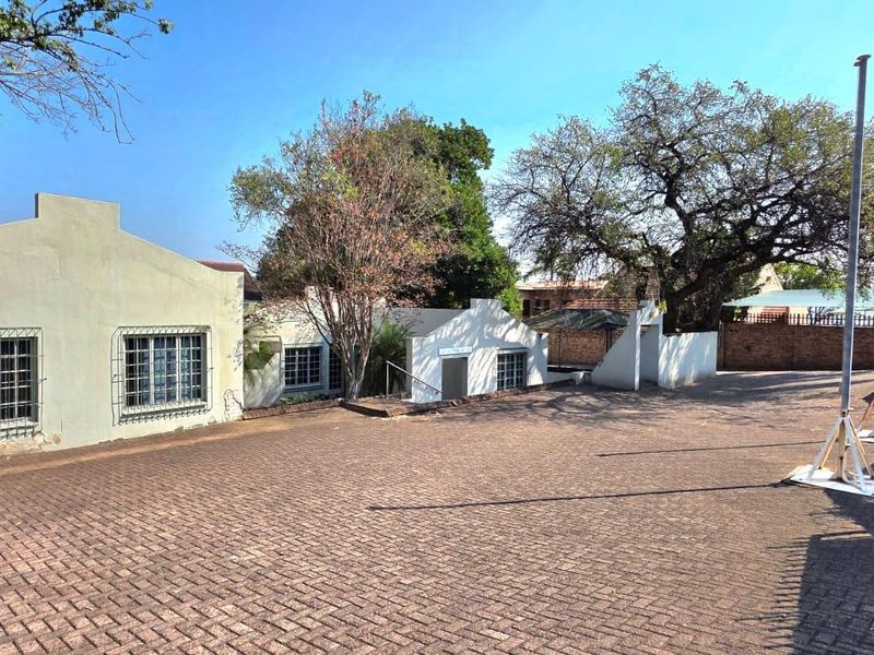 Exterior view of the office property featuring a large paved driveway, security-barred windows, and perimeter walling.