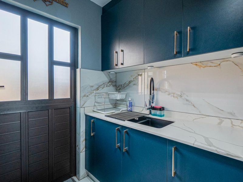 A modern, compact scullery featuring dark blue cabinetry, marble-look splashback, stone countertops, and a sleek undermount sink with a contemporary mixer tap.