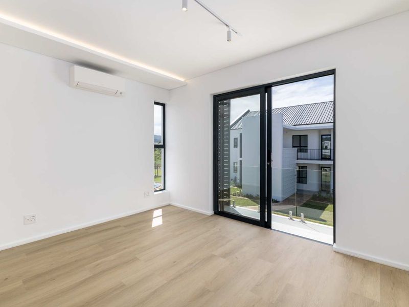 A bright, modern bedroom featuring light laminate flooring, a split-system air conditioner, and a sliding glass door leading to a private balcony.