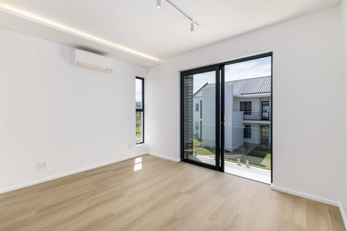 A bright, modern bedroom featuring light laminate flooring, a split-system air conditioner, and a sliding glass door leading to a private balcony.
