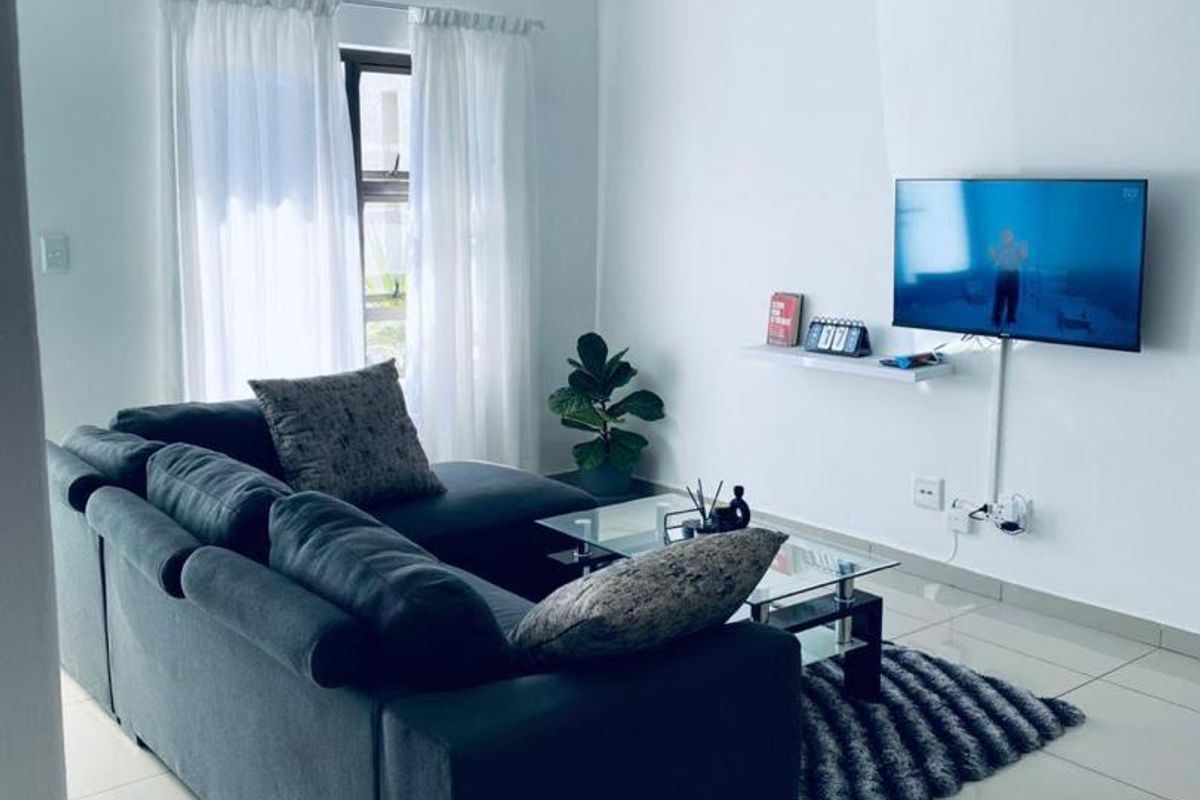 A bright living room featuring polished tiled flooring, coved ceiling cornices, and a wall-mounted floating shelf for media equipment.