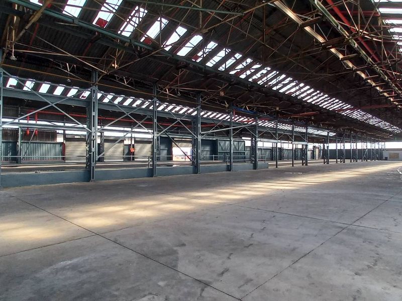 Expansive industrial warehouse space featuring high ceilings with exposed steel trusses, integrated skylights, and durable concrete flooring, suitable for various commercial or storage operations.