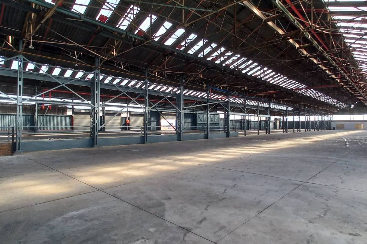 Expansive industrial warehouse space featuring high ceilings with exposed steel trusses, integrated skylights, and durable concrete flooring, suitable for various commercial or storage operations.