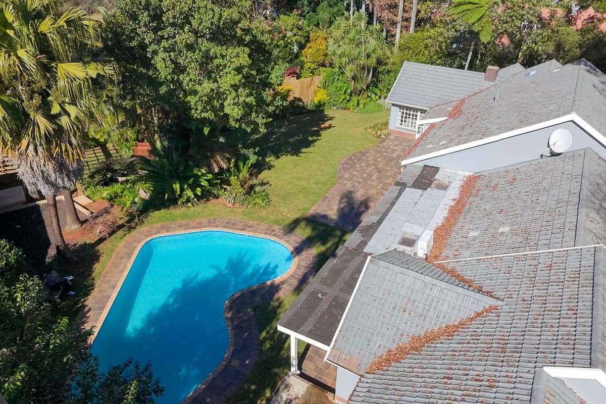 Aerial view of the property featuring a swimming pool, paved patio area, and a spacious garden with mature trees.