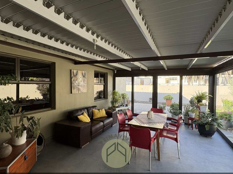 A spacious covered patio featuring a metal roof structure, paved flooring, and large sliding glass doors that provide seamless access to the garden area.