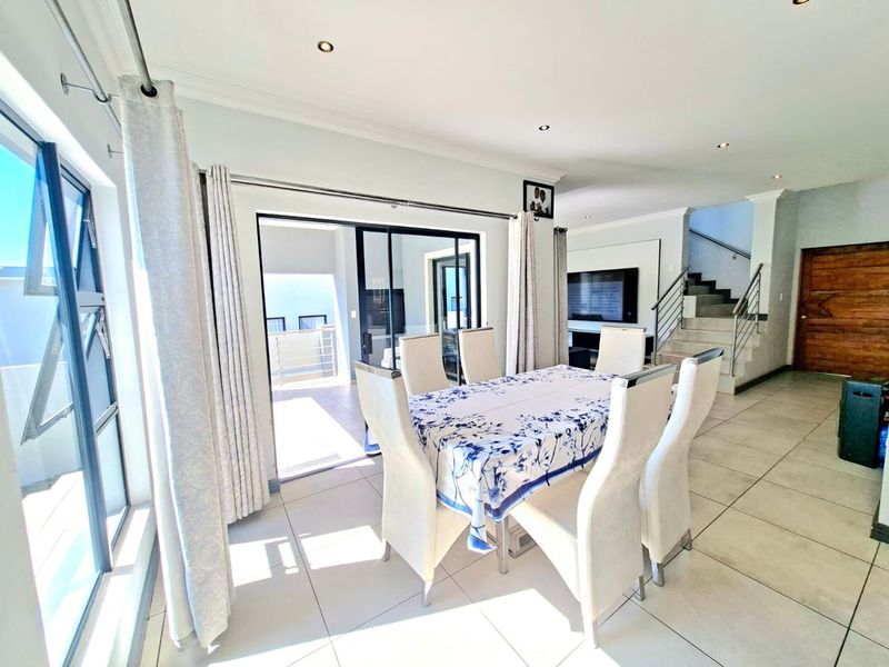 Bright open-plan dining area featuring large sliding doors to the patio, tiled flooring, recessed lighting, and a modern staircase with a metal balustrade.