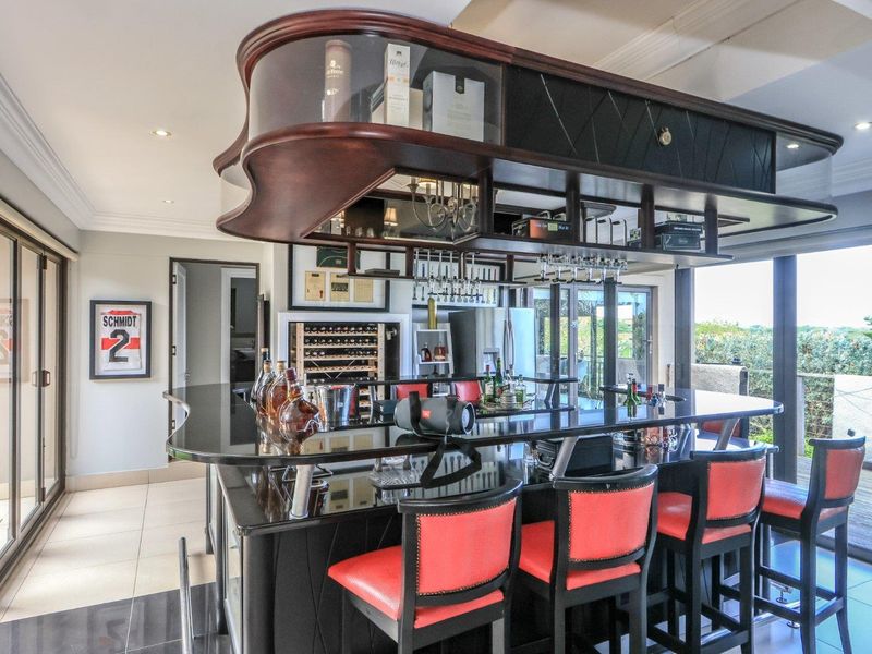 A sophisticated built-in bar area featuring a dark stone counter, overhead glass storage, and integrated wine refrigeration, opening onto an outdoor patio.