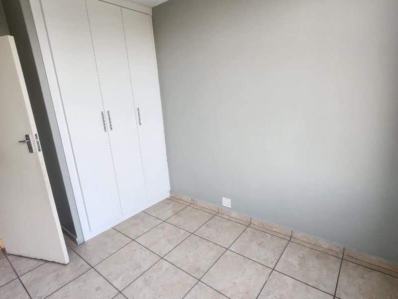 A vacant bedroom featuring neutral wall paint, tiled flooring, and a built-in wardrobe with white cabinetry.