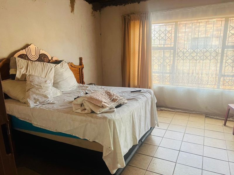 A bedroom featuring tiled flooring and security bars on the window, currently showing significant signs of wear and damage to the walls and ceiling.