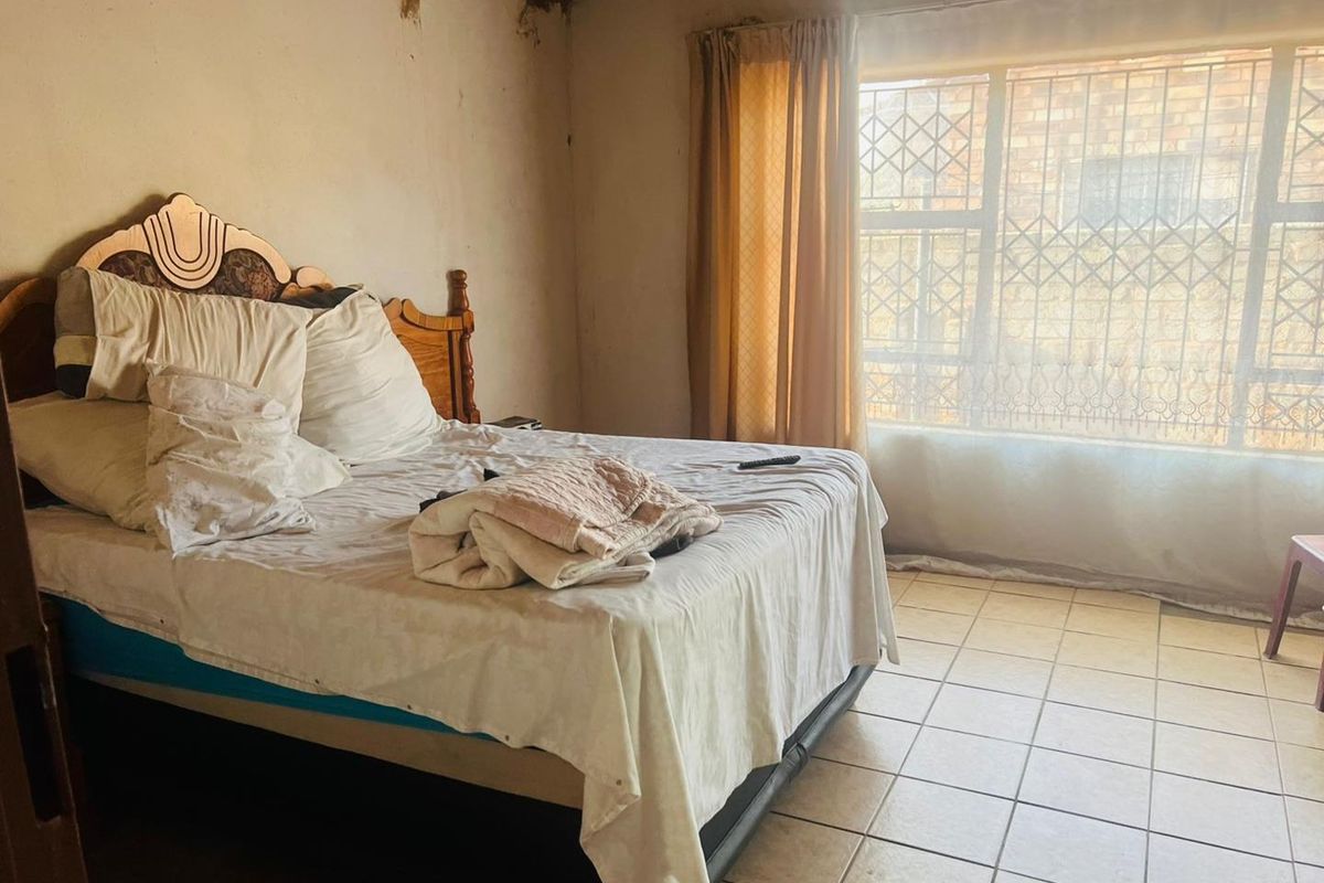 A bedroom featuring tiled flooring and security bars on the window, currently showing significant signs of wear and damage to the walls and ceiling.
