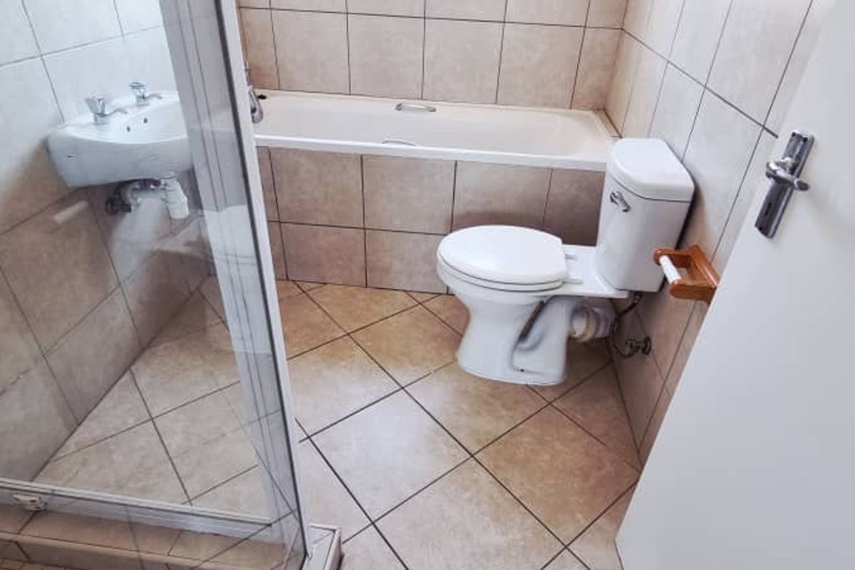A functional bathroom featuring a tiled shower enclosure, a built-in bathtub, and a standard toilet with ceramic floor tiles.