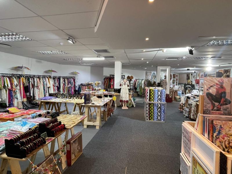 A spacious open-plan retail interior featuring a suspended ceiling with recessed lighting and carpeted flooring, currently utilized as a clothing and gift shop.
