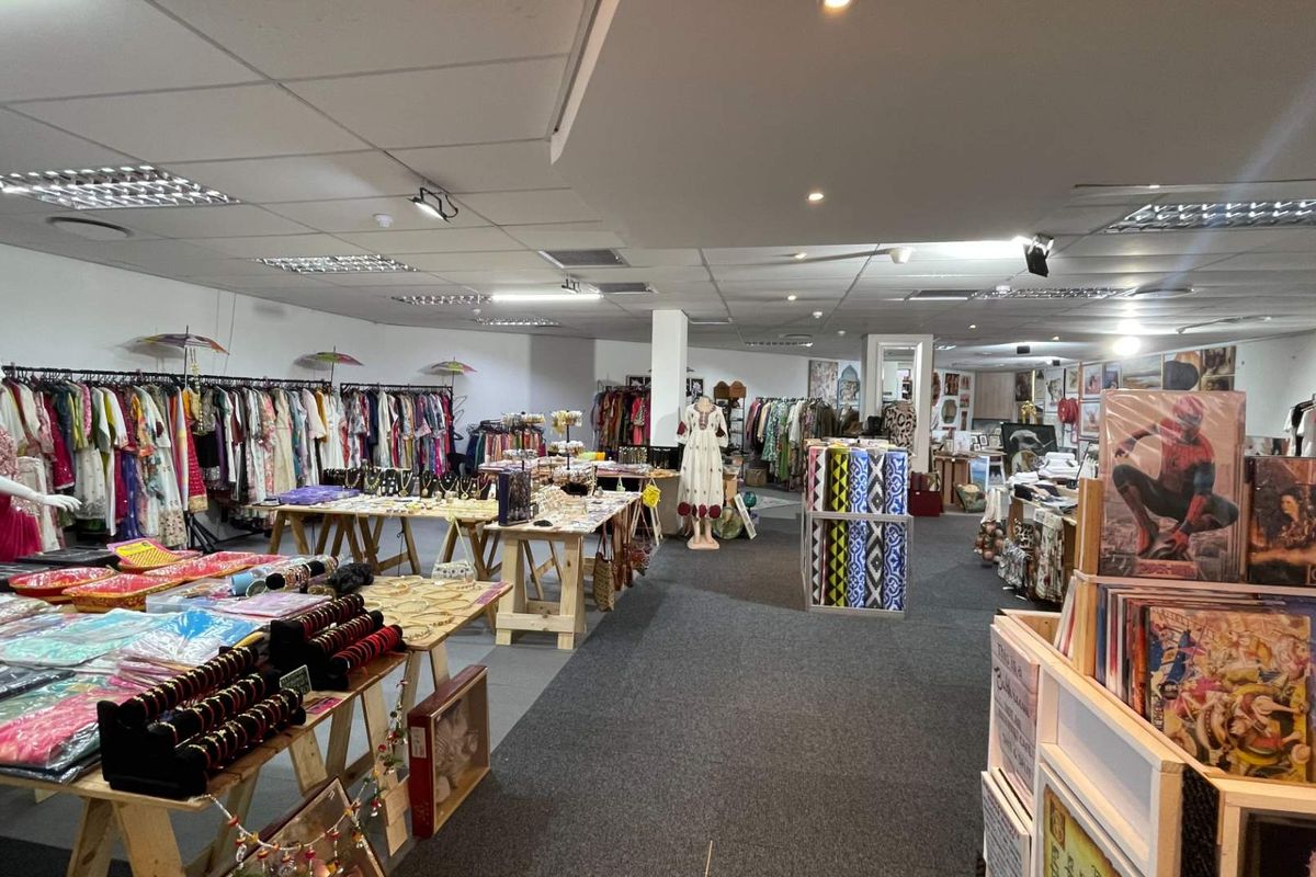 A spacious open-plan retail interior featuring a suspended ceiling with recessed lighting and carpeted flooring, currently utilized as a clothing and gift shop.