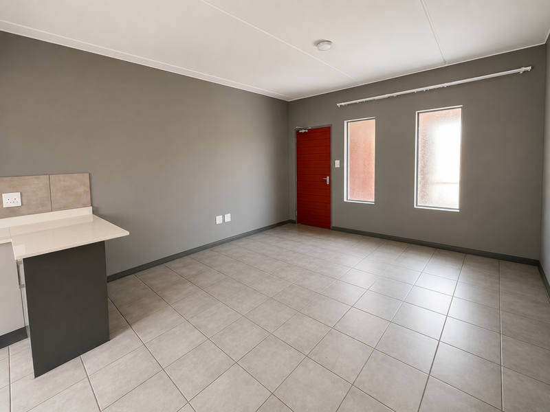 An open-plan living area featuring neutral grey walls, tiled flooring, a modern stone-topped kitchen counter, and a distinctive red entrance door.