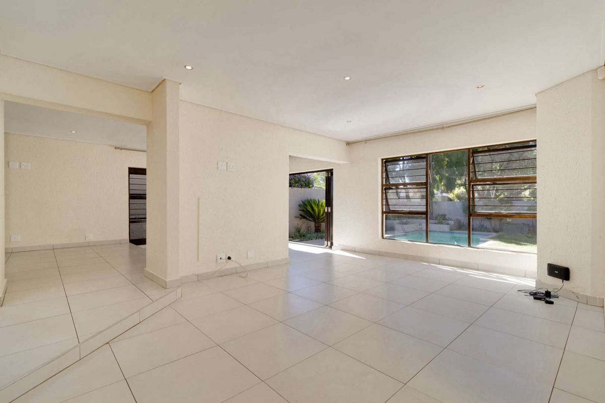 Spacious, light-filled living area featuring neutral tiled flooring, recessed lighting, and large windows with views of the outdoor pool area.