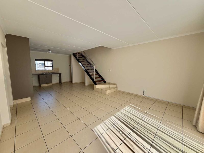 Spacious open-plan living area featuring tiled flooring, a modern staircase with metal railings, and a functional kitchen corner with built-in cabinetry.