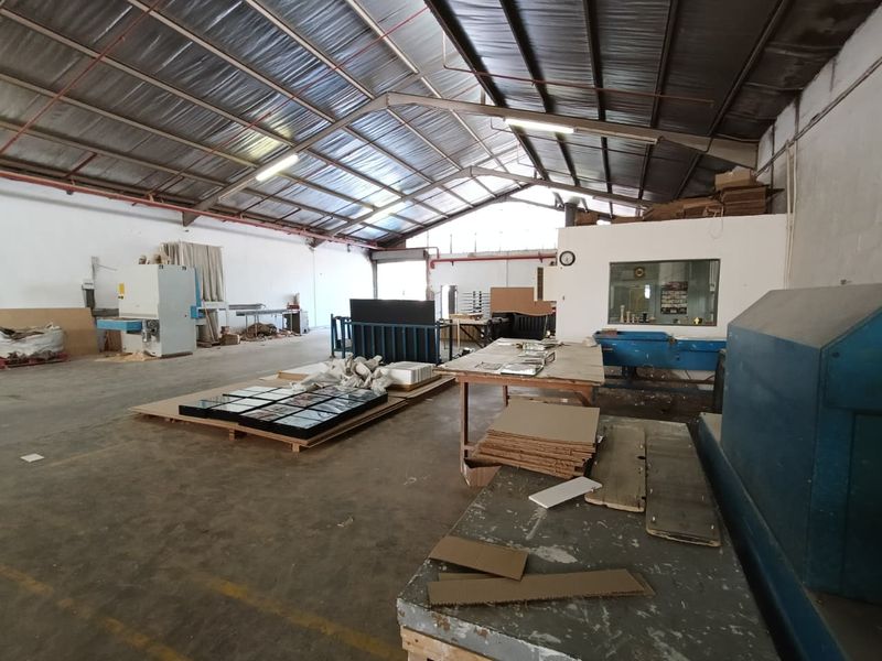 Spacious industrial warehouse area featuring high exposed steel roof trusses, concrete flooring, and an integrated internal office partition.