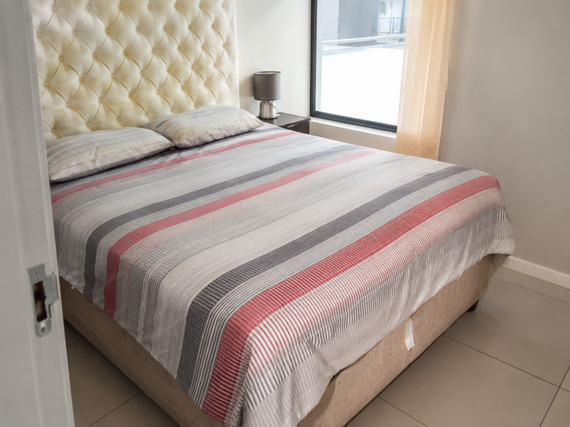 A well-maintained bedroom featuring neutral tiled flooring and a large window that allows for natural light.
