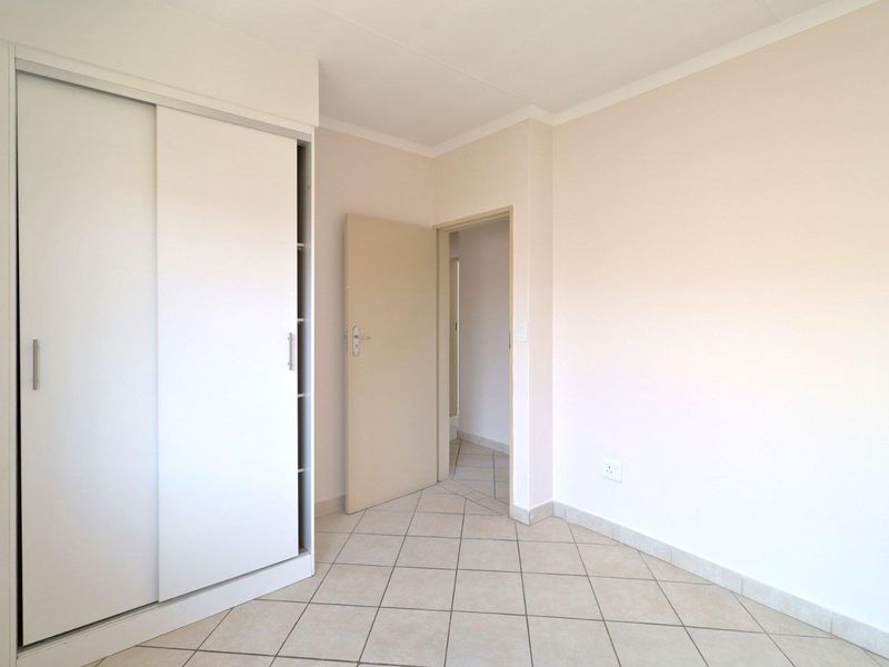 A clean, empty bedroom featuring neutral tiled flooring, a built-in sliding door wardrobe, and a simple doorway leading to an adjacent space.