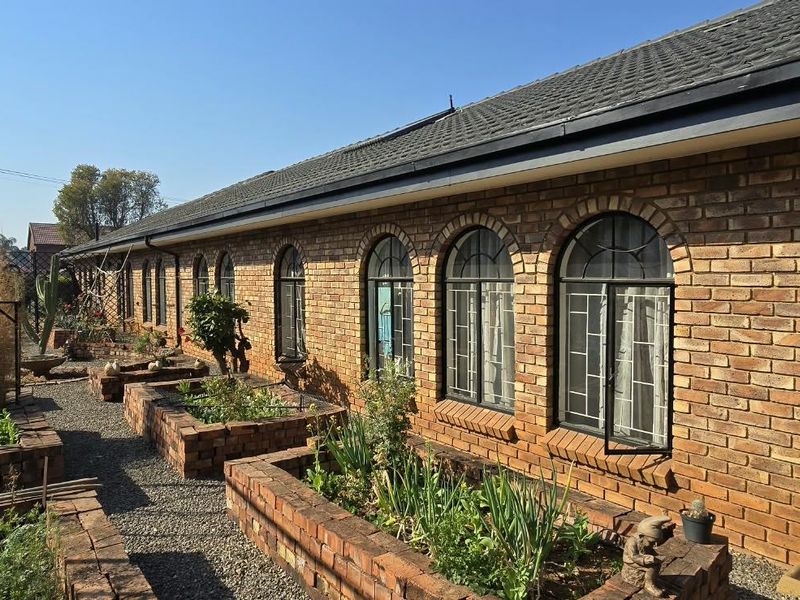 Rear exterior view of a face brick house featuring arched windows, security bars, and established raised brick garden beds.