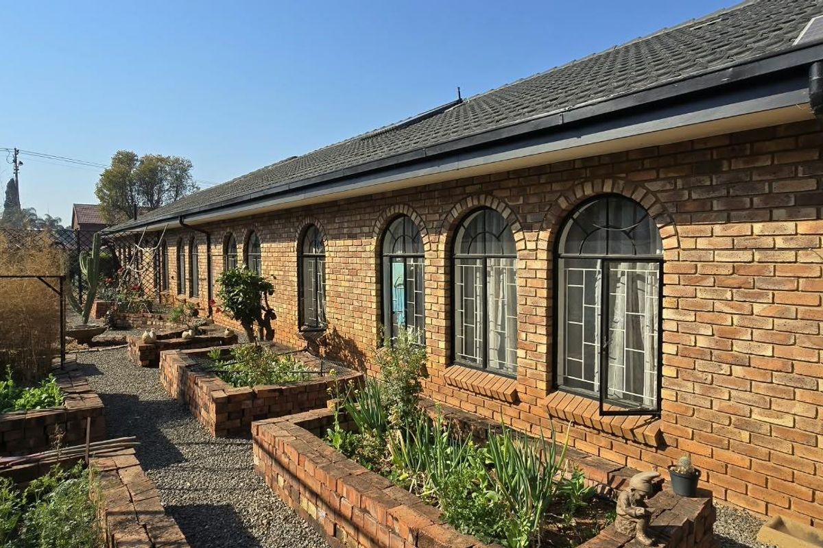 Rear exterior view of a face brick house featuring arched windows, security bars, and established raised brick garden beds.