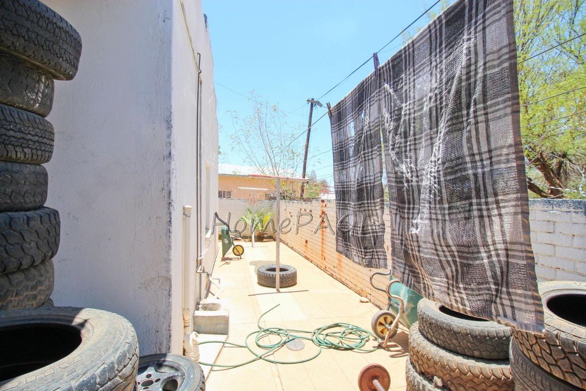 A side exterior area featuring paved ground, a boundary wall, and external plumbing fixtures, currently utilized as a utility and storage space.