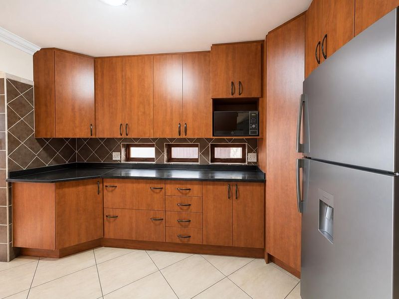 A clean, functional kitchen featuring warm-toned laminate cabinetry, dark granite countertops, a tiled backsplash, and neutral ceramic floor tiles.