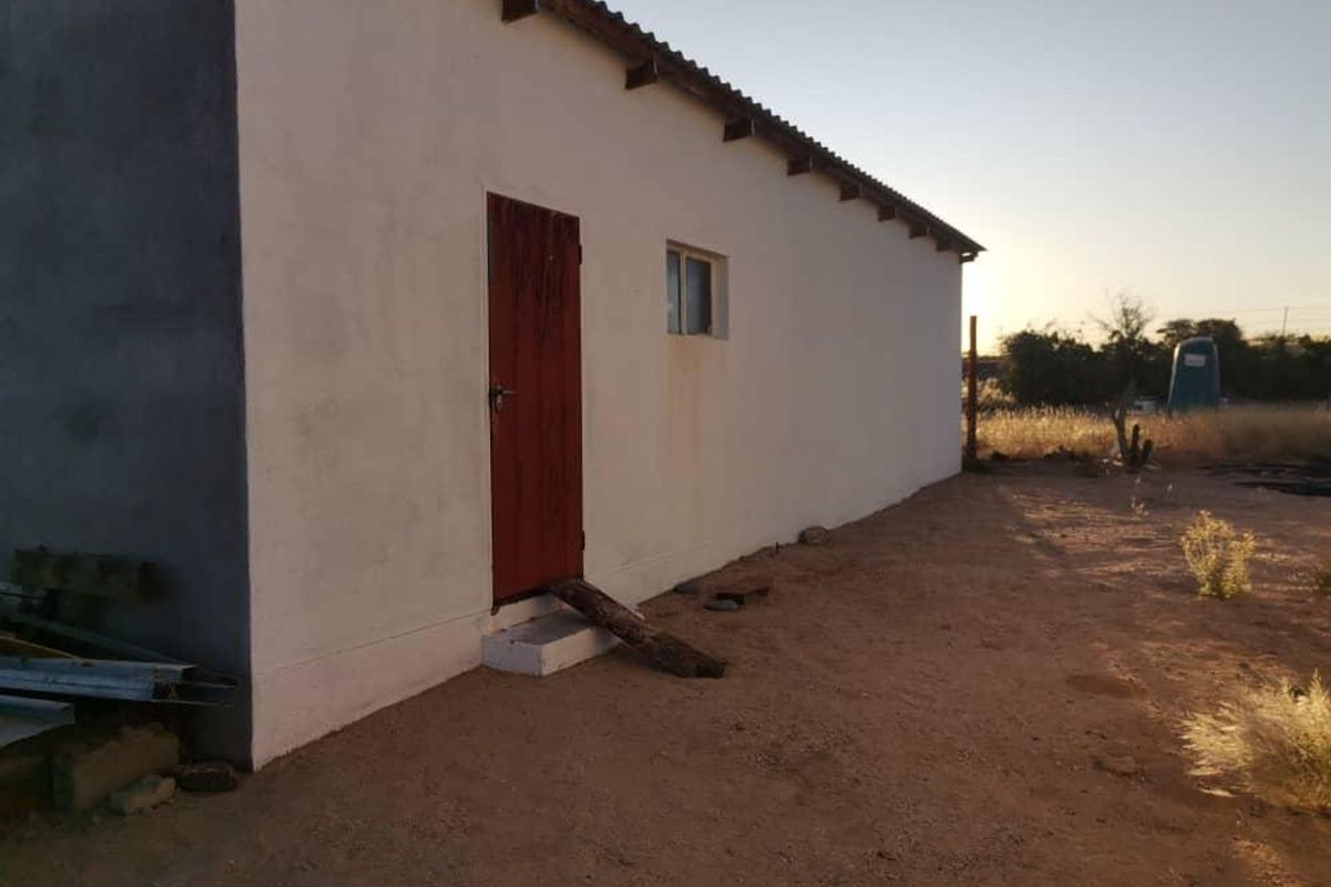 Side view of a small holding structure featuring a simple plastered exterior, corrugated roof sheeting, and a single access door.