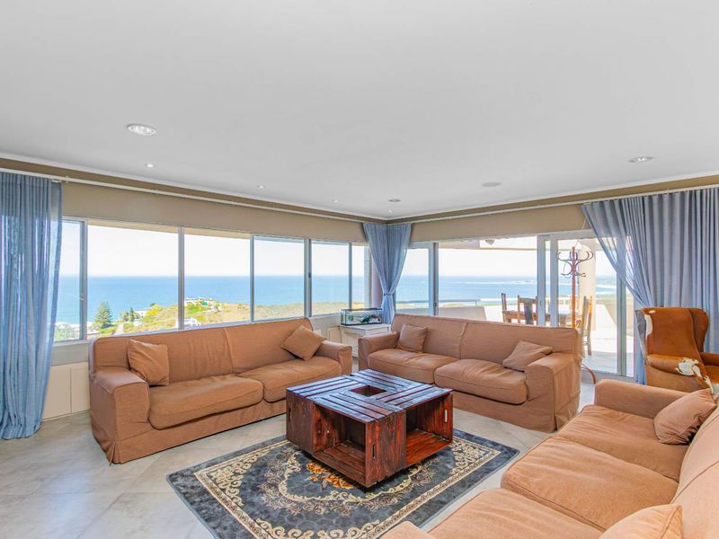 Spacious living room featuring expansive floor-to-ceiling windows with panoramic ocean views and direct access to an outdoor patio area.