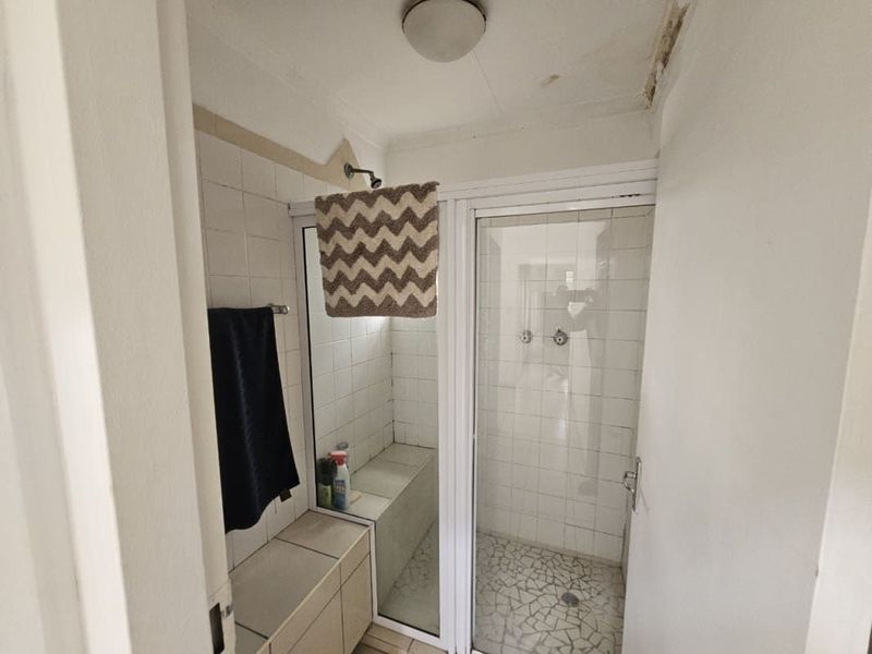 A functional bathroom featuring a tiled shower enclosure with a built-in bench, showing signs of ceiling water damage requiring maintenance.