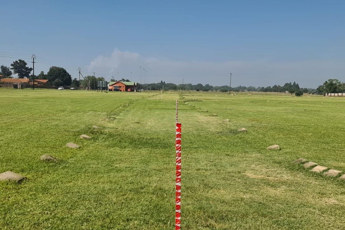 A wide-angle view of a vacant agricultural land plot featuring open grassy terrain and boundary markers.
