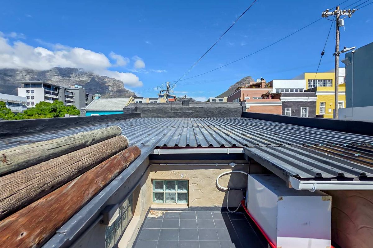An elevated rear exterior view showing a corrugated metal roof, tiled terrace area, and glass block window with mountain views in the background.