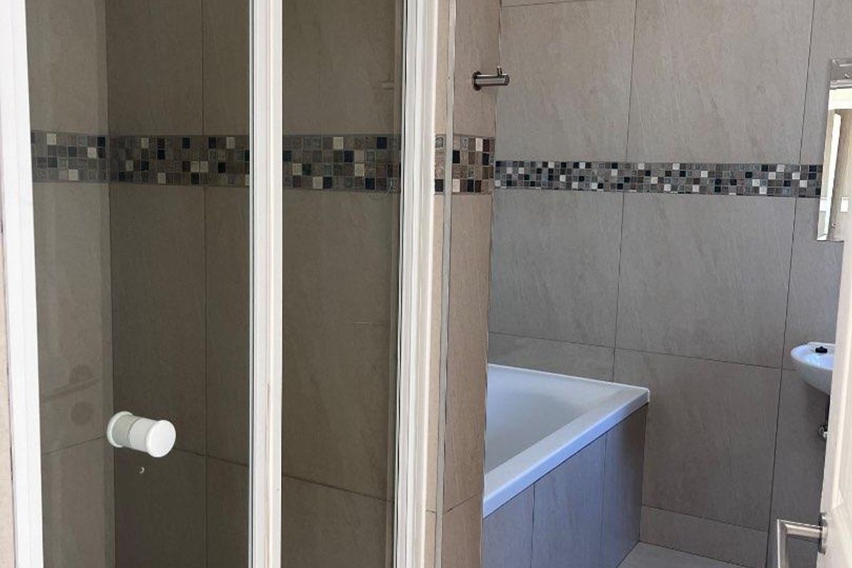 A modern bathroom featuring a glass-enclosed shower, a built-in bathtub, and neutral wall tiling with a decorative mosaic accent border.