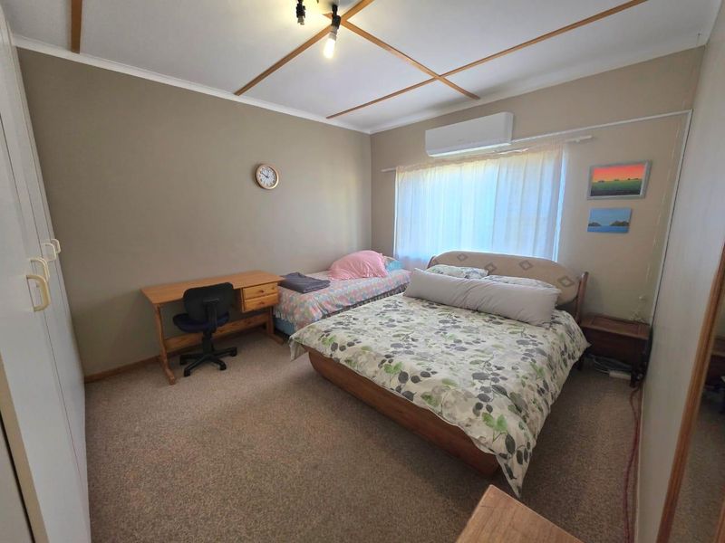 A functional bedroom featuring carpeted flooring, built-in cupboards, and a wall-mounted split-system air conditioner for climate control.
