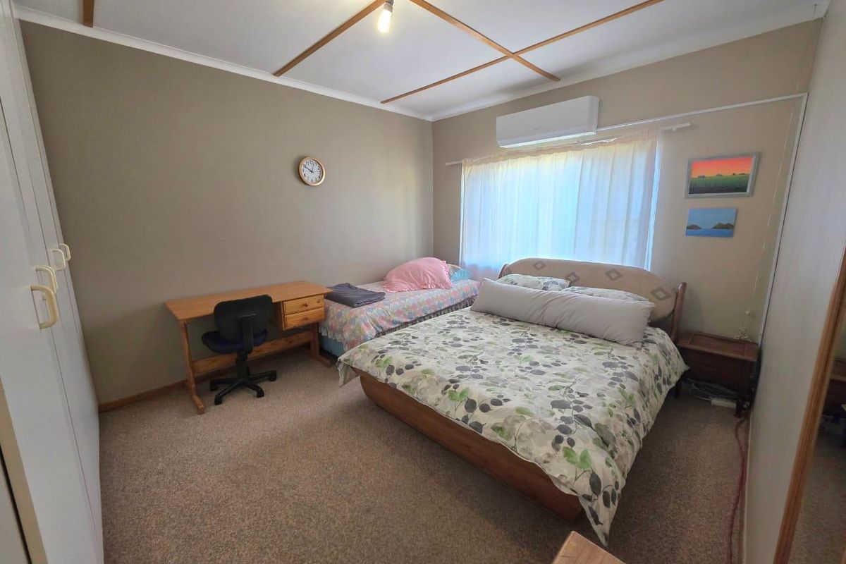 A functional bedroom featuring carpeted flooring, built-in cupboards, and a wall-mounted split-system air conditioner for climate control.