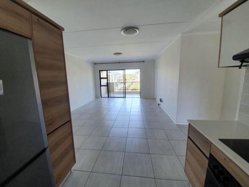 Spacious open-plan living area featuring modern wood-finish cabinetry, tiled flooring, and direct access to a private balcony through sliding glass doors.