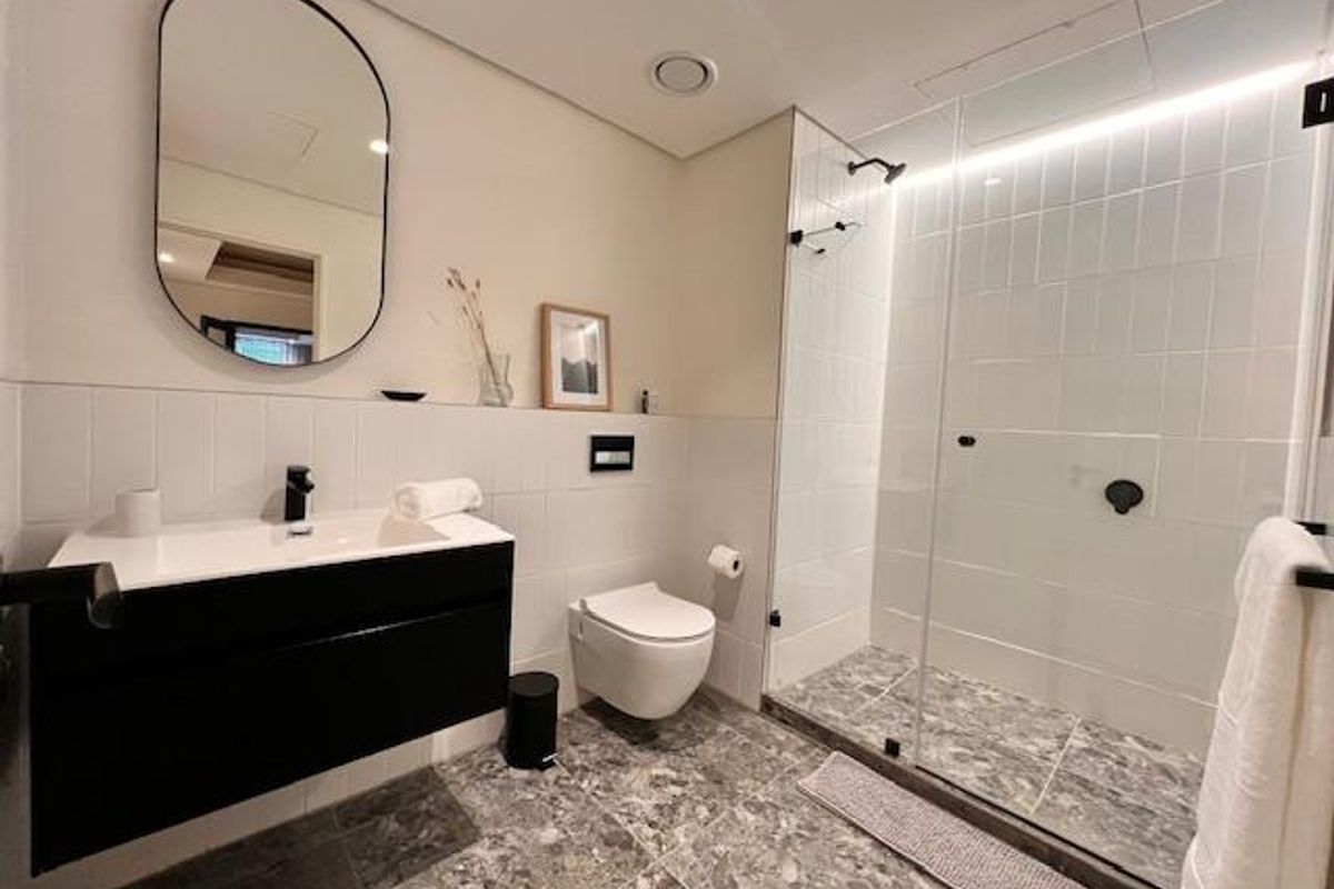 Modern bathroom featuring a floating vanity, wall-mounted toilet, and a spacious walk-in shower with glass enclosure and integrated lighting.