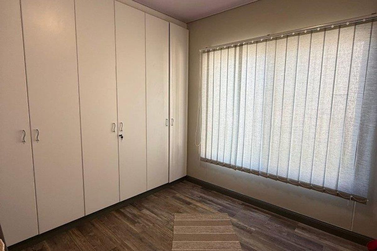 A bedroom featuring built-in floor-to-ceiling wardrobes, wood-look laminate flooring, and vertical window blinds.