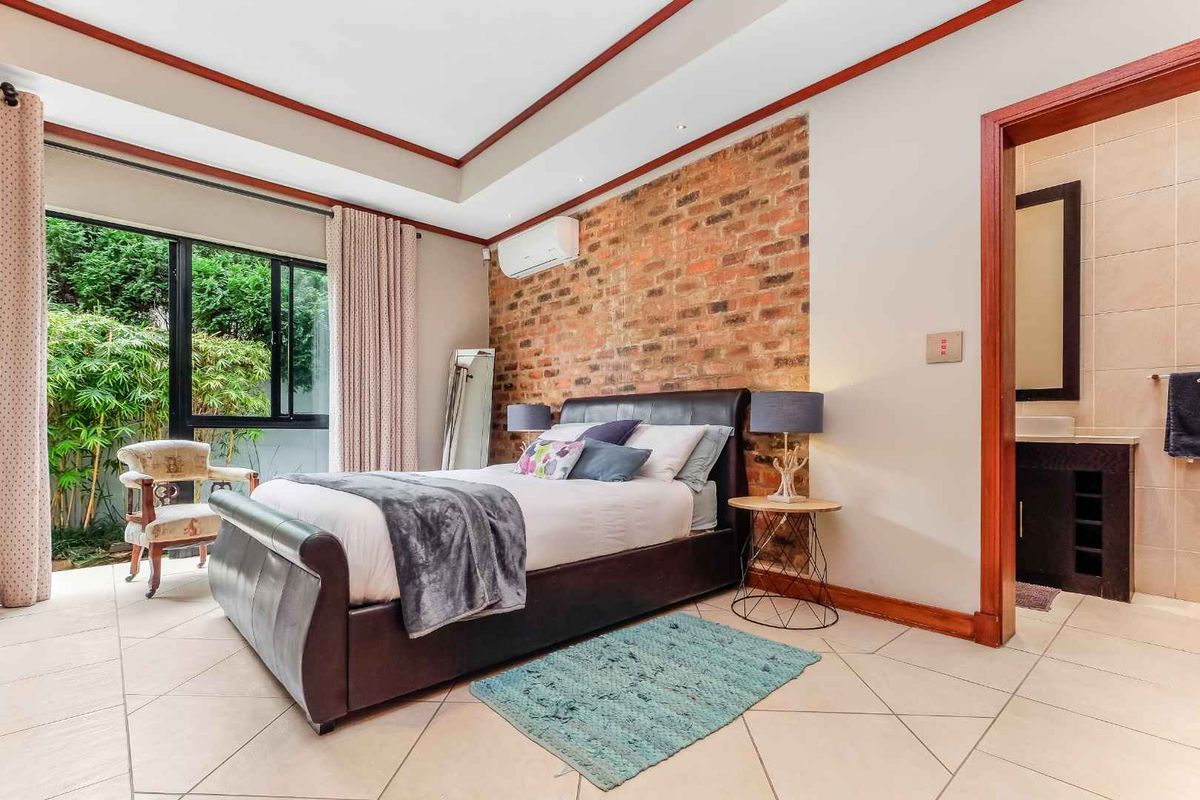 Spacious bedroom featuring an exposed brick feature wall, tiled flooring, split-system air conditioning, and direct access to an en-suite bathroom.