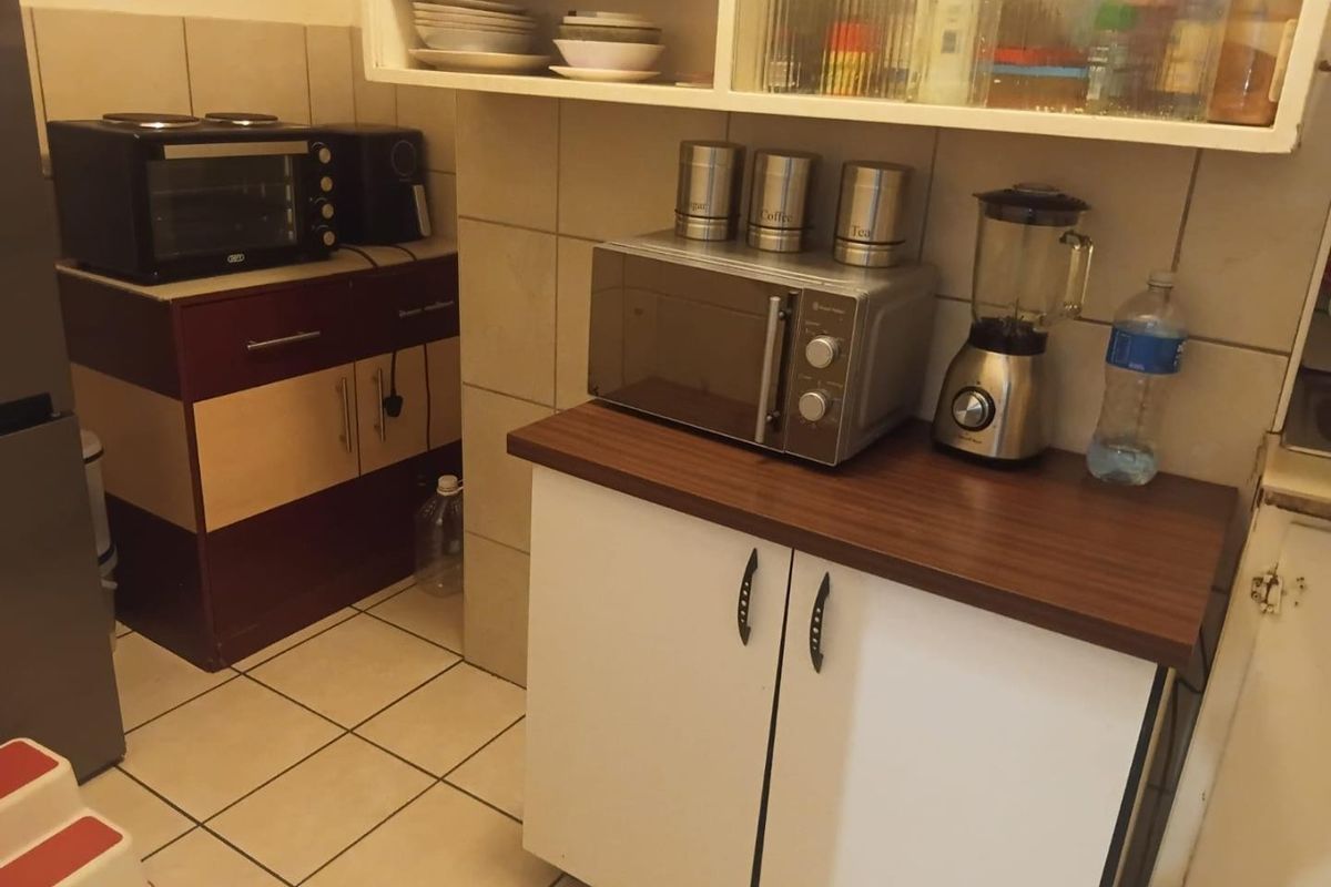A functional kitchen area featuring tiled flooring, a tiled backsplash, built-in cabinetry with laminate countertops, and convenient wall-mounted shelving for storage.