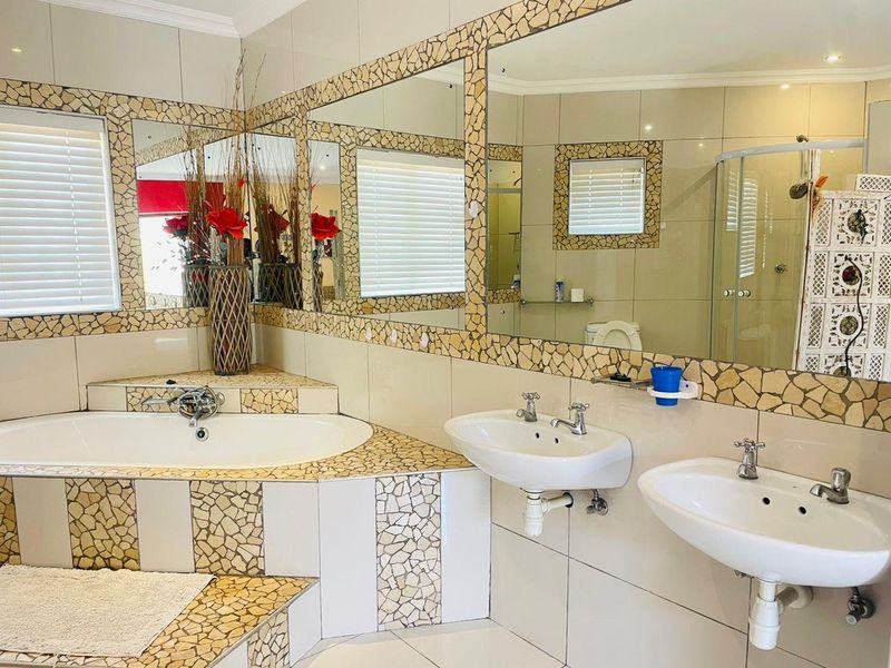 Spacious bathroom featuring a corner bathtub, dual washbasins, and a glass shower enclosure with distinctive mosaic tile detailing.