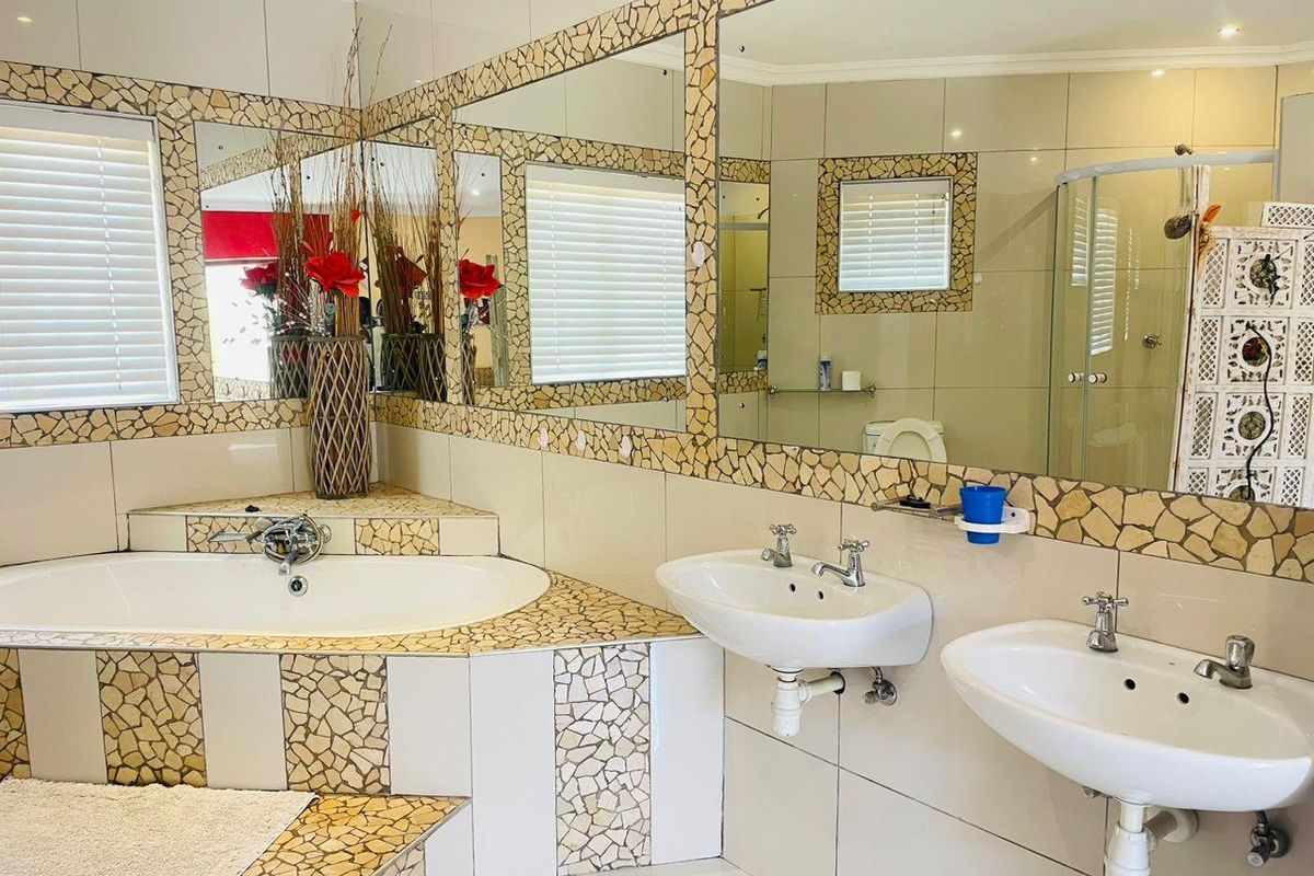 Spacious bathroom featuring a corner bathtub, dual washbasins, and a glass shower enclosure with distinctive mosaic tile detailing.