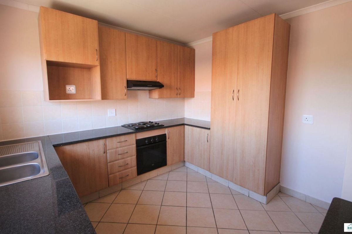 A clean and functional kitchen featuring light wood-finish cabinetry, dark granite countertops, a built-in oven with gas hob, and tiled flooring.