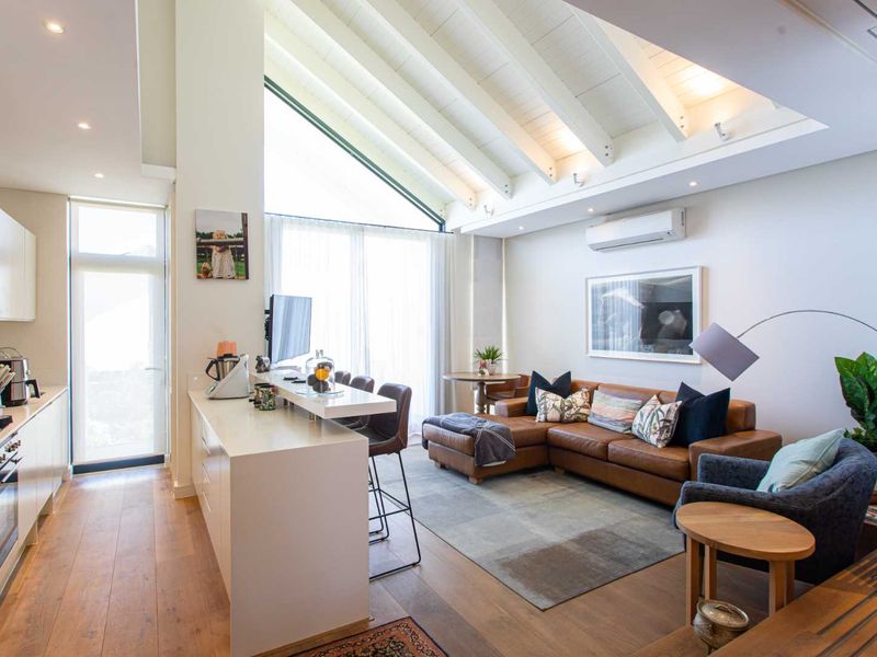Modern open-plan living area featuring a sleek kitchen with integrated appliances, high vaulted ceilings with exposed beams, and warm timber flooring.