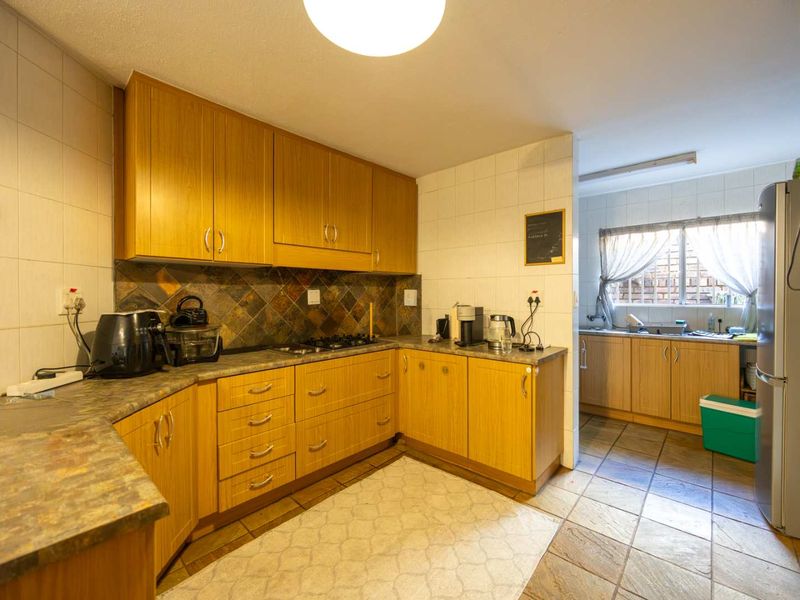 A functional kitchen featuring wood-look cabinetry, stone-effect countertops, and a tiled backsplash, with an adjoining scullery area providing additional workspace and sink facilities.